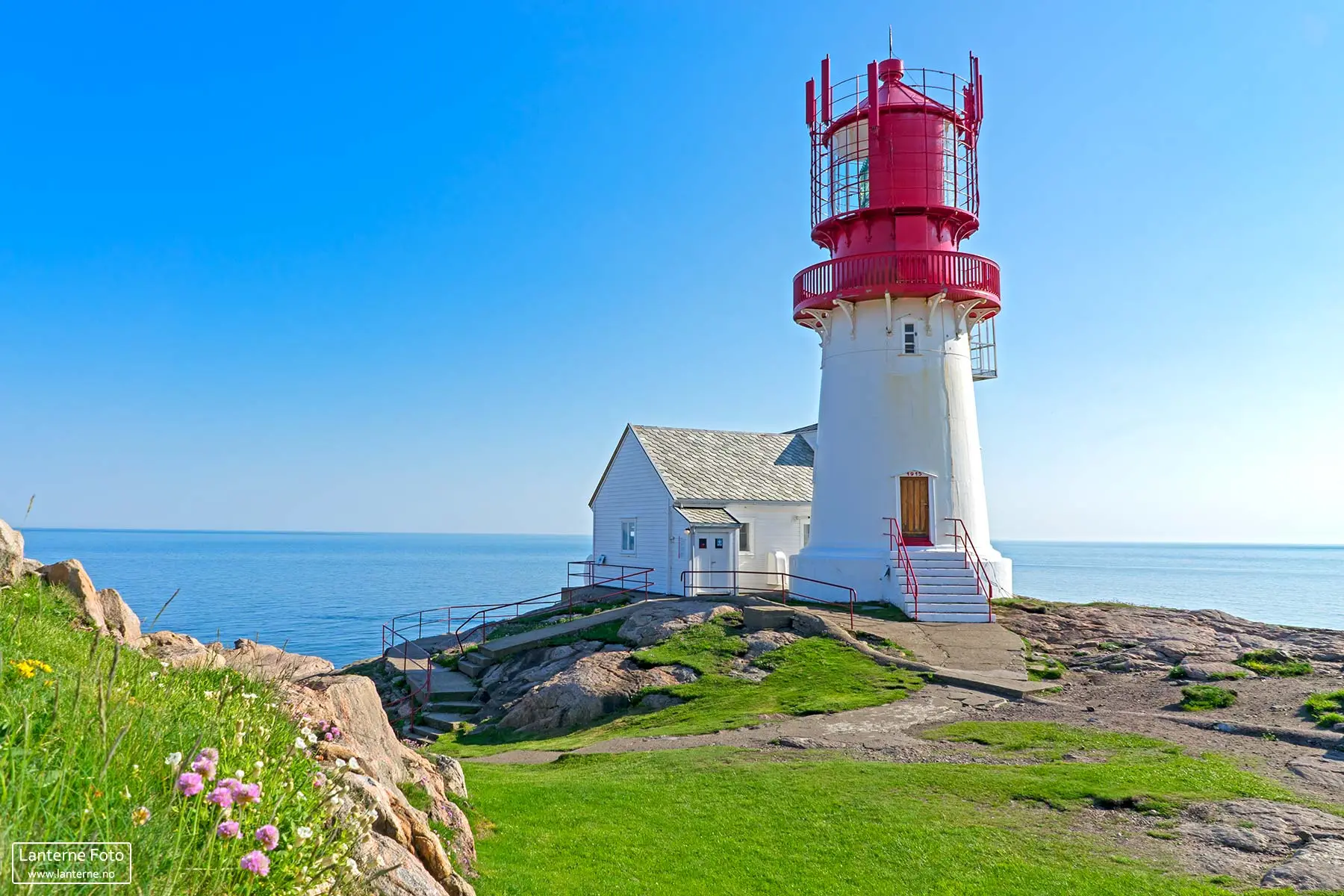 Lindesnes fyr med rødt tårn og hvit bygning på sommerdag