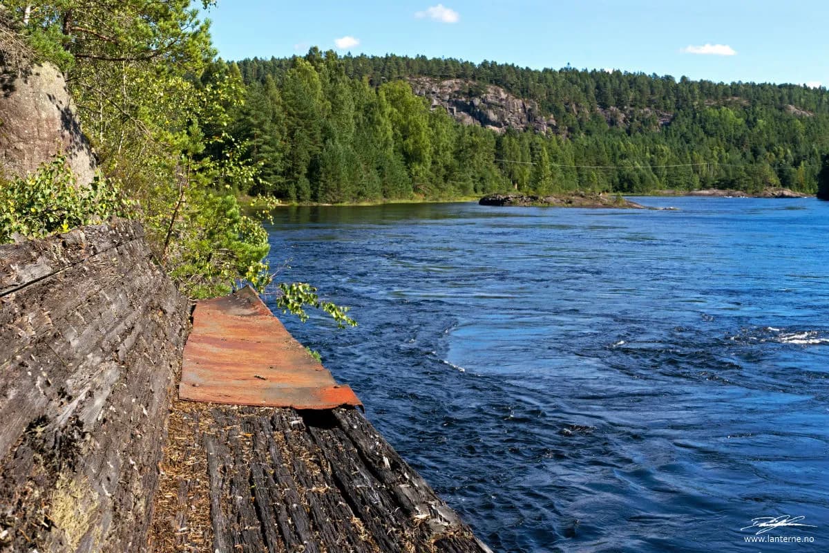 Tømmerrenna ender ved Otra med skogkledde åser i bakgrunnen